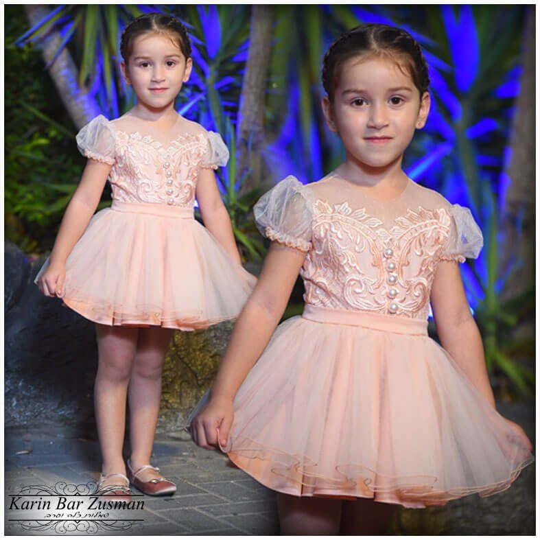 ילדה בשמלת טוטו ורודה מחייכת, בחוץ ליד צמחים.