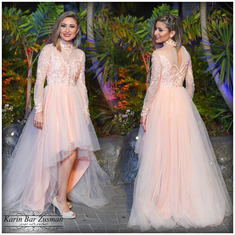 אישה בשמלה רשמית בצבע אפרסק עם שרוולים ארוכים ומכפלת גבוהה-נמוכה. היא מחייכת, מצטלמת בחוץ.