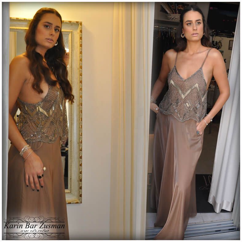 אישה בשמלה חומה משובצת חרוזים עומדת ליד פתח, מצטלמת מול מראה.