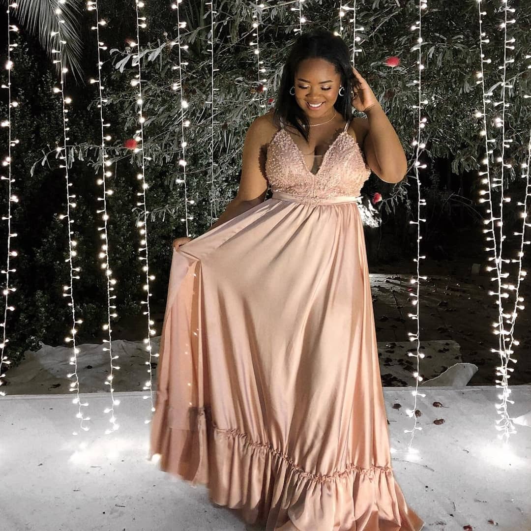 אישה בשמלה בצבע סומק מחייכת. היא עומדת בחוץ מול שרשרת אורות.