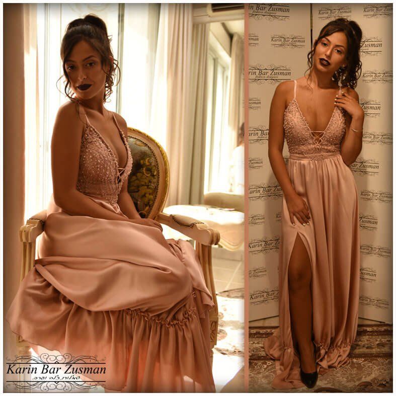 אישה בשמלה בצבע ורוד עם מחוך משובץ חרוזים, פוזת ליד חלון ועומדת עם שס גבוה.