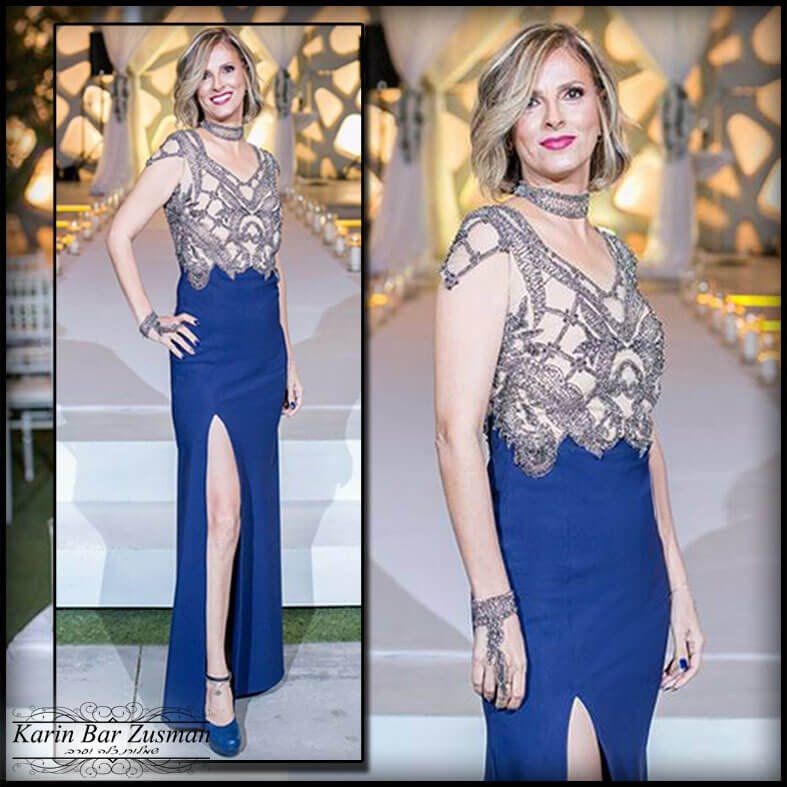 אישה בשמלה כחולה עם חלק עליון משובץ חרוזים, מצטלמת על שביל לבן.