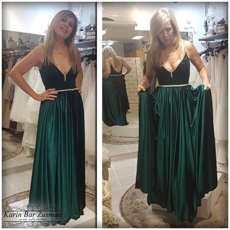 אישה בשמלה ירוקה אזמרגד, מצטלמת בחנות כלות, מחייכת כשזרועותיה על הירכיים.