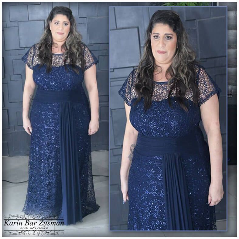 אישה בשמלת ערב כחולה כהה עם מחוך תחרה, עומדת מול קיר מרוצף.