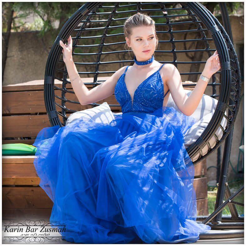 אישה בלבוש רשמי כחול, יושבת בכיסא תלוי, ידיים מורמות, בחוץ.