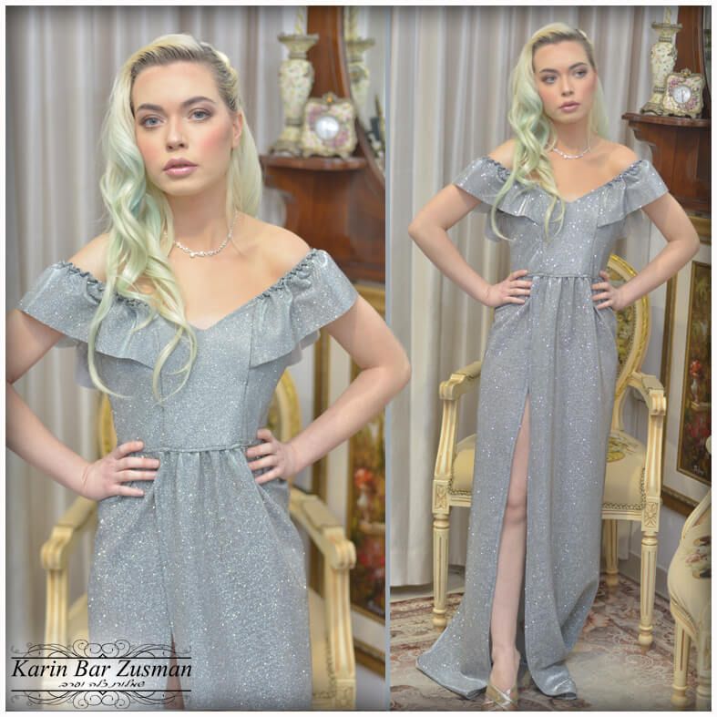 אישה בשמלה כסופה, חשופה כתפיים עם שס גבוה, מצטלמת בתוך הבית.