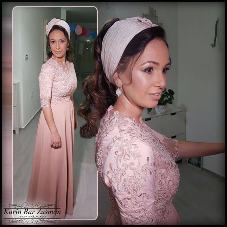 אישה בשמלה ורודה וכיסוי ראש, מצטלמת. בתוך הבית, עם איפור אלגנטי ותספורת.