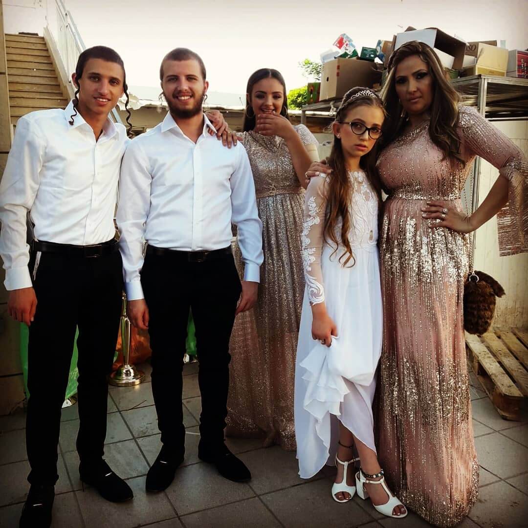 קבוצה של שישה אנשים מצטלמים בחוץ; שני גברים בחולצות לבנות, שלוש נשים בשמלות וילדה בשמלה לבנה.