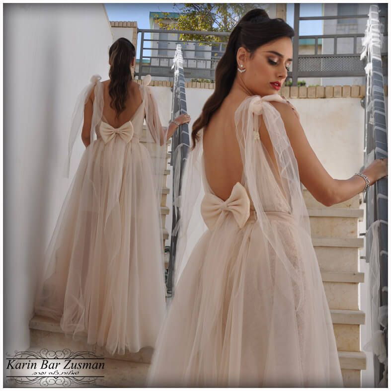 אישה בשמלת טול בצבע קרם עם עיטור קשת, עומדת על מדרגות.