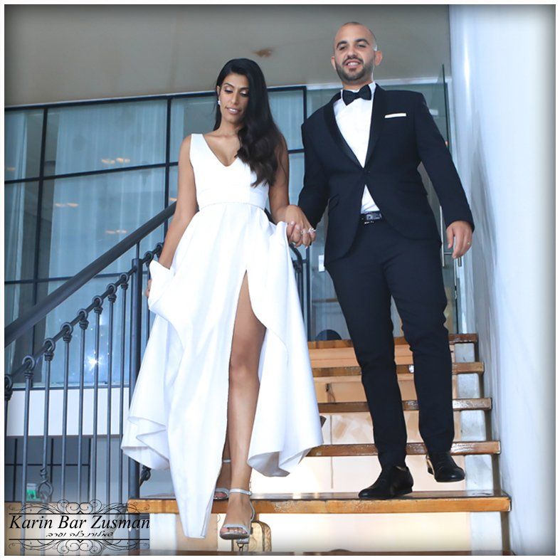 חתן וכלה יורדים במדרגות, היא בשמלה לבנה עם שס, הוא בחליפה שחורה, שניהם אוחזים ידיים.