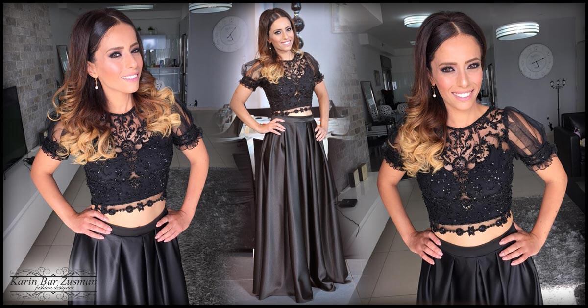 אישה בטופ וחצאית תחרה שחורה, ידיים על הירכיים, מחייכת.