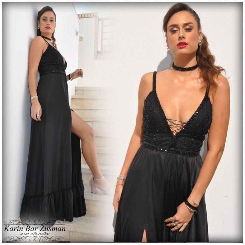 אישה בשמלת ערב שחורה עם שס גבוה, מצטלמת על מדרגות, רקע לבן.