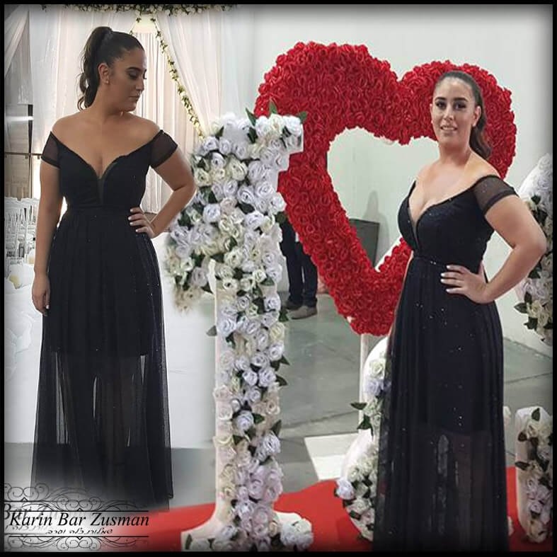 אישה בשמלה שחורה עם קישוטי פרחים, מצטלמת באירוע.