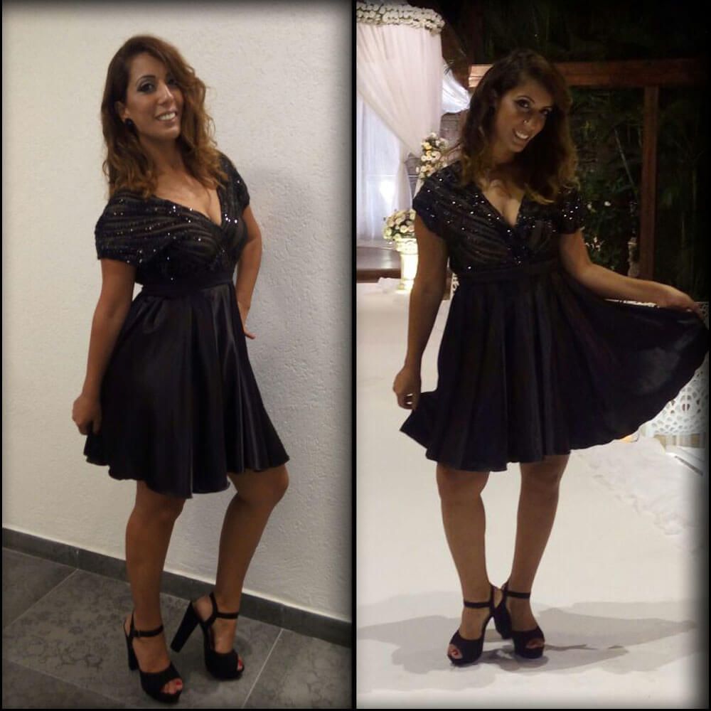 אישה בשמלה שחורה ועקבים, מצטלמת בתוך הבית עם חיוך.