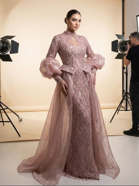 אישה בשמלה ורודה מעוטרת עם שרוולים נפוחים ושובץ, מצטלמת בסטודיו עם צלם.