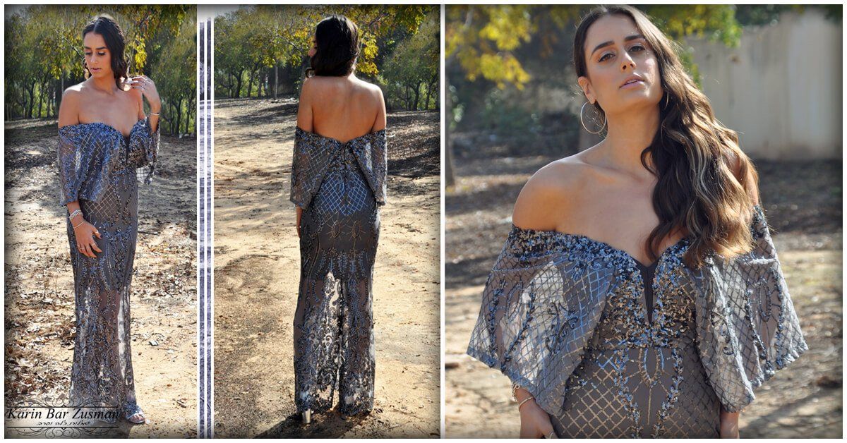 אישה בשמלה כסופה נוצצת ללא כתפיים מצטלמת בחוץ עם עצים ברקע.