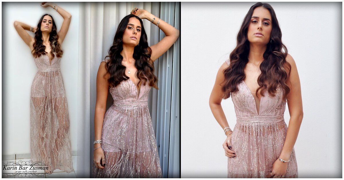 אישה בשמלה ורודה נוצצת, מצטלמת עם ידיים מורמות וידיים על הירכיים, בתוך הבית.