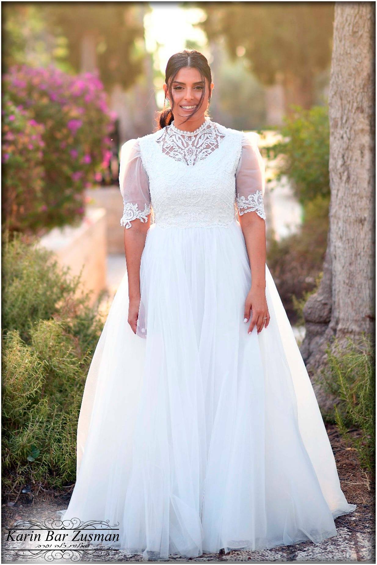 אישה בשמלת כלה לבנה, עומדת בחוץ, מחייכת.