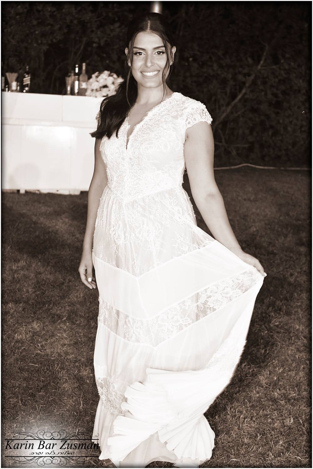 אישה בשמלת תחרה לבנה, מחייכת, אוחזת חצאית בחוץ, גוון ספיה.