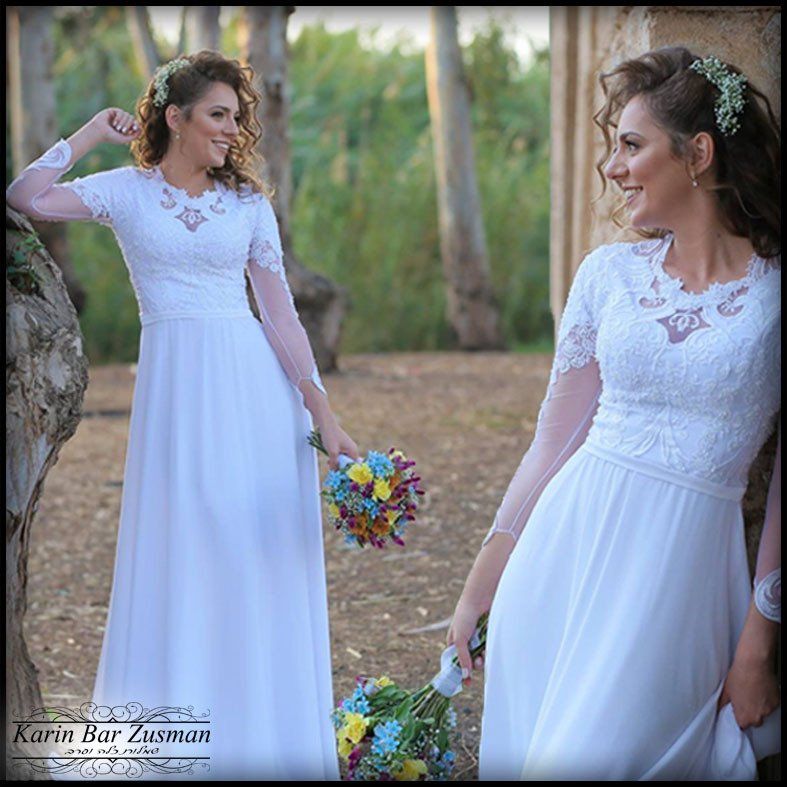 אישה בשמלת כלה לבנה אוחזת בפרחים, מחייכת בסביבה טבעית בחיק הטבע.