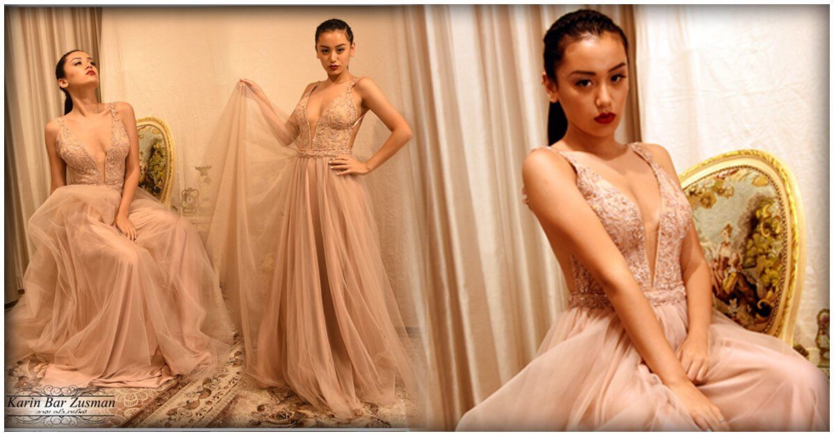 אישה בשמלה בצבע סומק מצטלמת בתוך הבית. היא יושבת, עומדת ומביטה למצלמה. תאורה רכה, רקע ניטרלי.