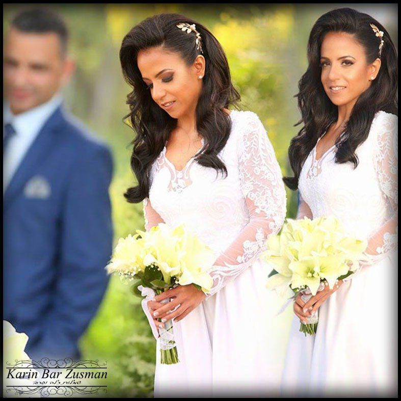 שתי נשים בשמלות לבנות אוחזות זרי פרחים; גבר בחליפה כחולה מטושטש ברקע.