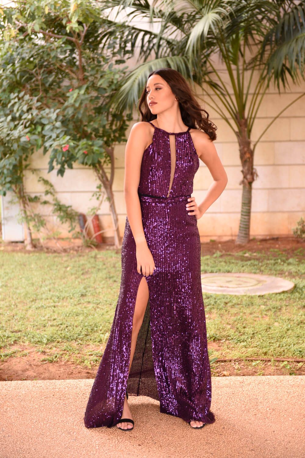 אישה בשמלת נצנצים סגולה מצטלמת בחוץ, יד על הירך, רגל שסופה.