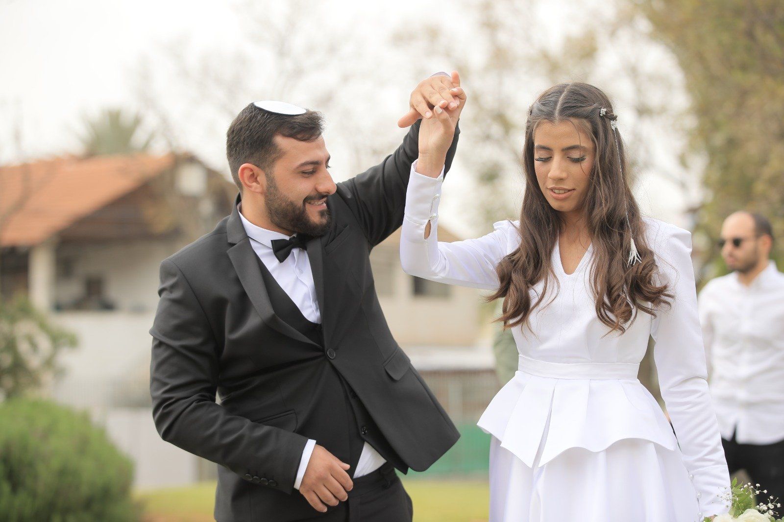זוג טרי רוקד בחוץ; החתן לובש חליפה, הכלה שמלה לבנה.