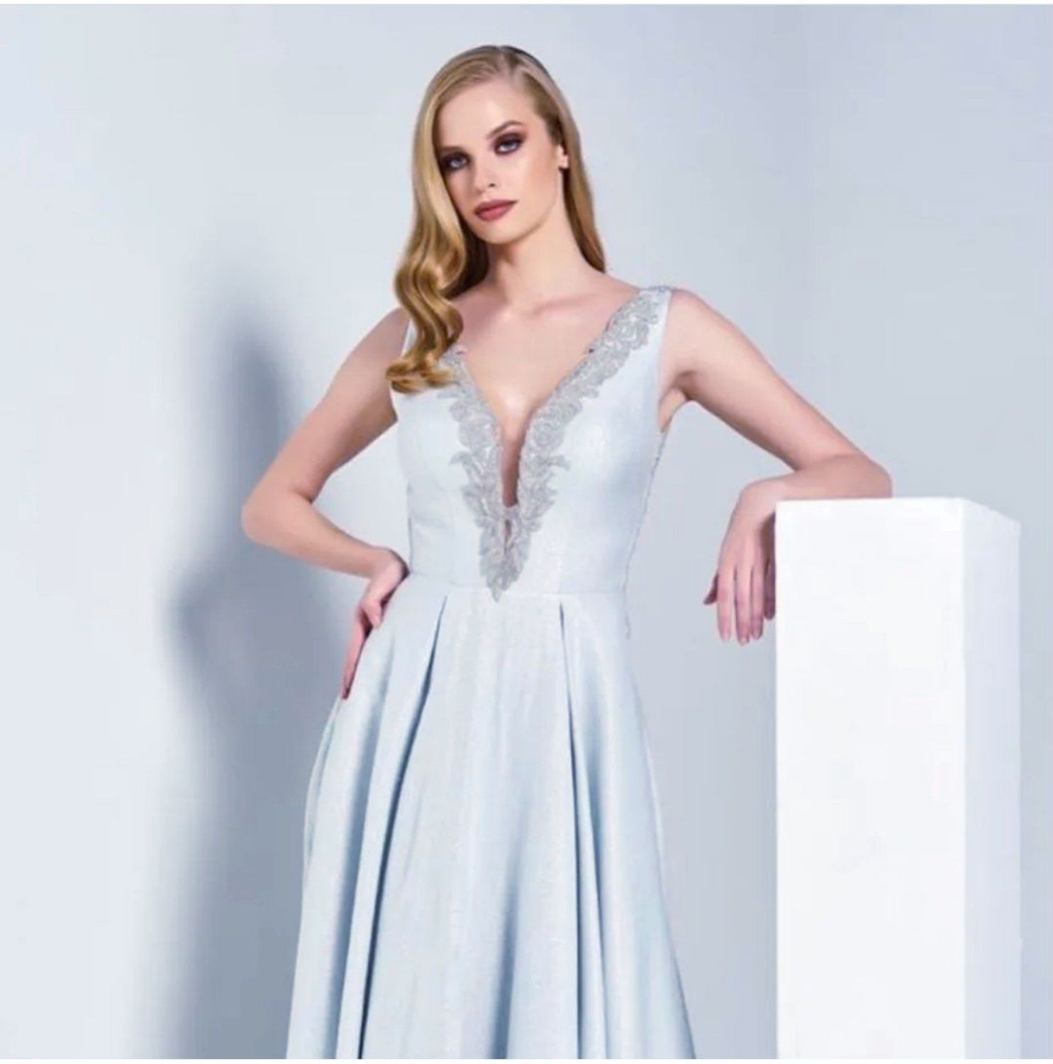 אישה בשמלה רשמית תכלת, ידיים על הירכיים, נשענת על עמוד לבן.