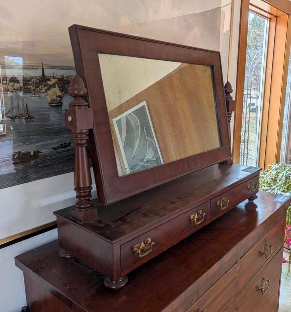 A dark wood vanity mirror with three small drawers, resting on top of a larger dresser.