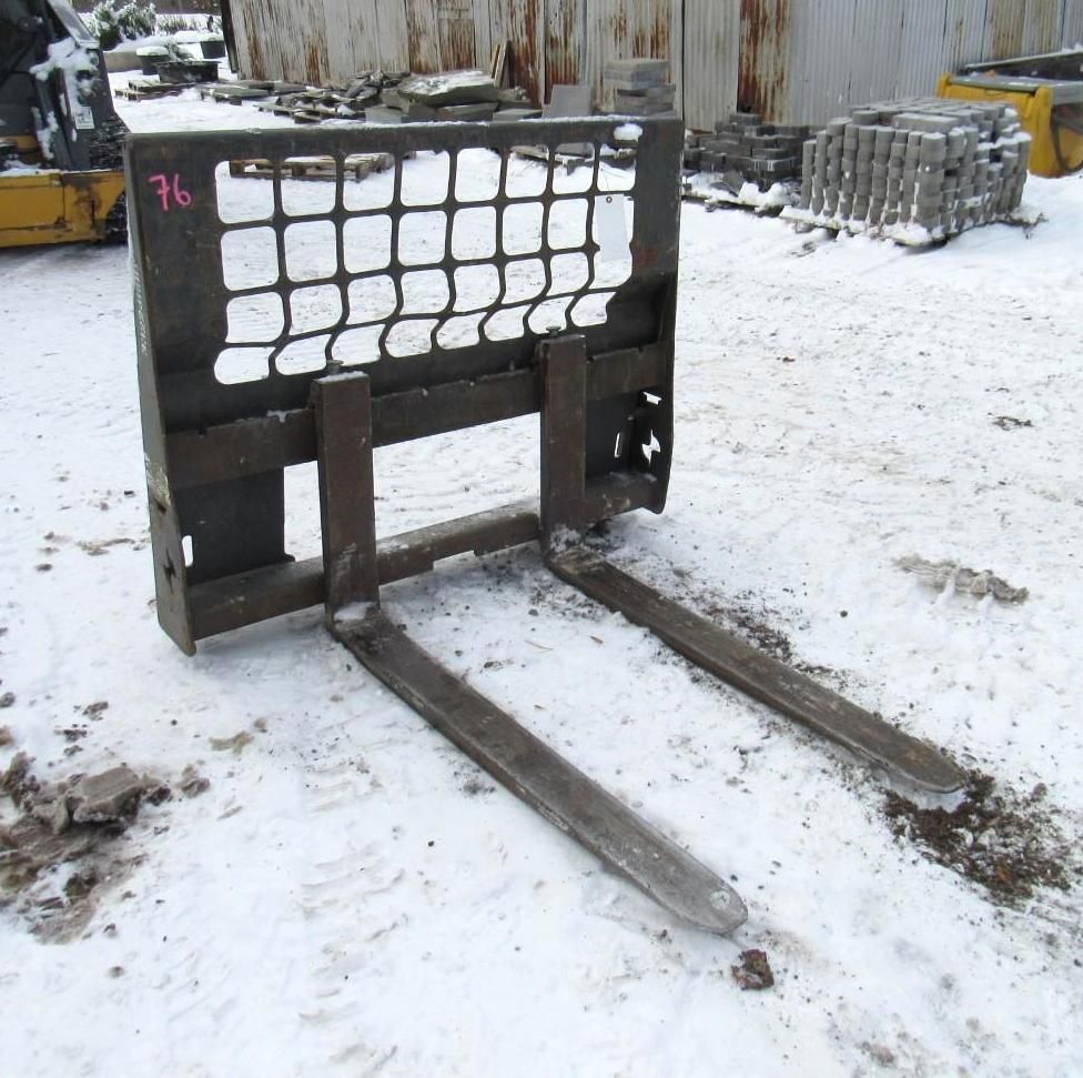 Skid steer forklift attachment with metal forks, resting in snow.