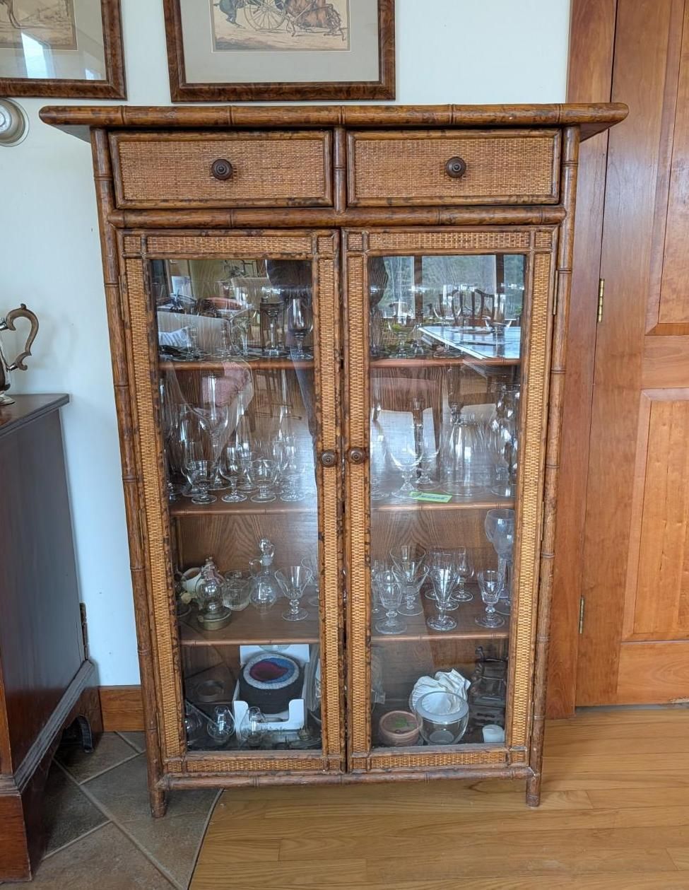A tall, Victorian-style bamboo cabinet with two drawers and two glass-paneled doors containing glass display items.