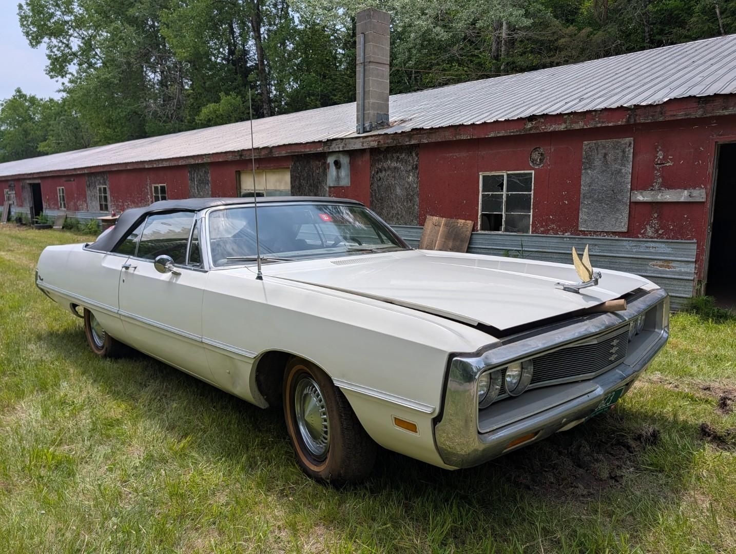 Vintage white coupe parked beside a red brick building and grass.