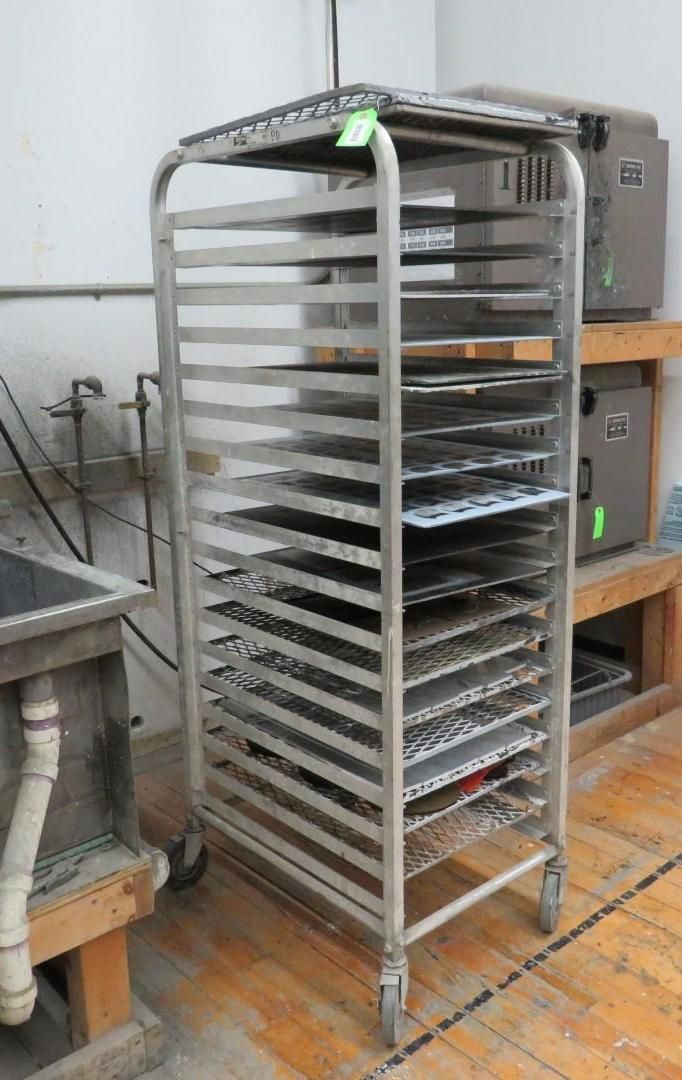 A stainless steel rack on wheels filled with trays, in a workshop setting.