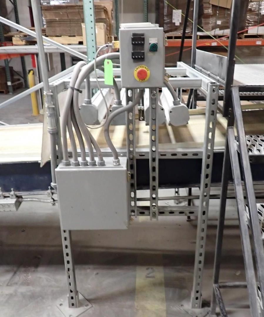 Gray electrical control box and wiring mounted on industrial metal frame over a conveyor belt.