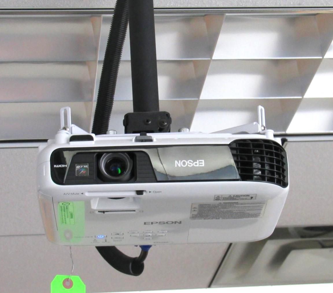 White Epson projector, mounted on ceiling with black cable, projecting.