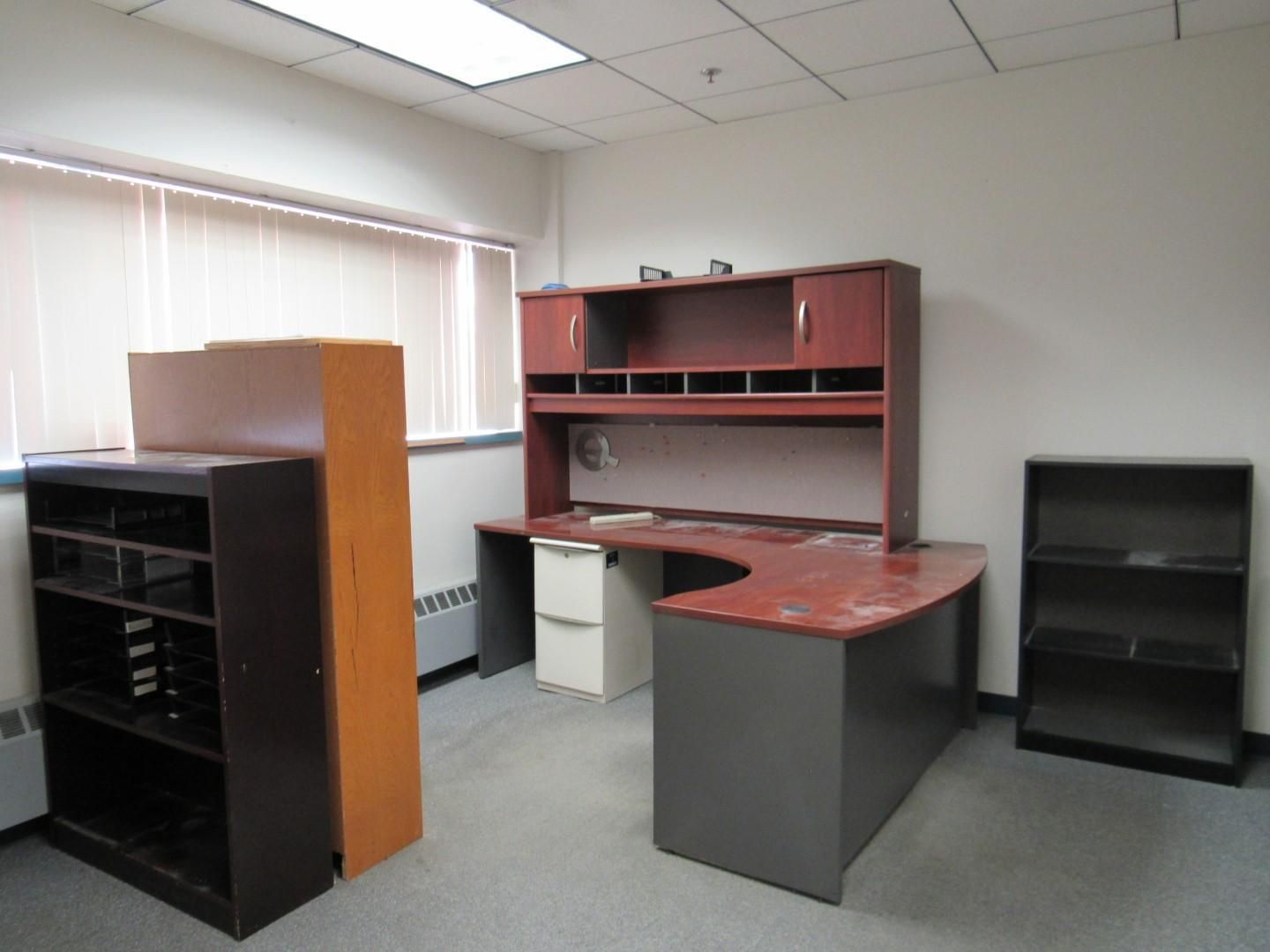 Office space with an empty desk, bookshelves, and a window with blinds.
