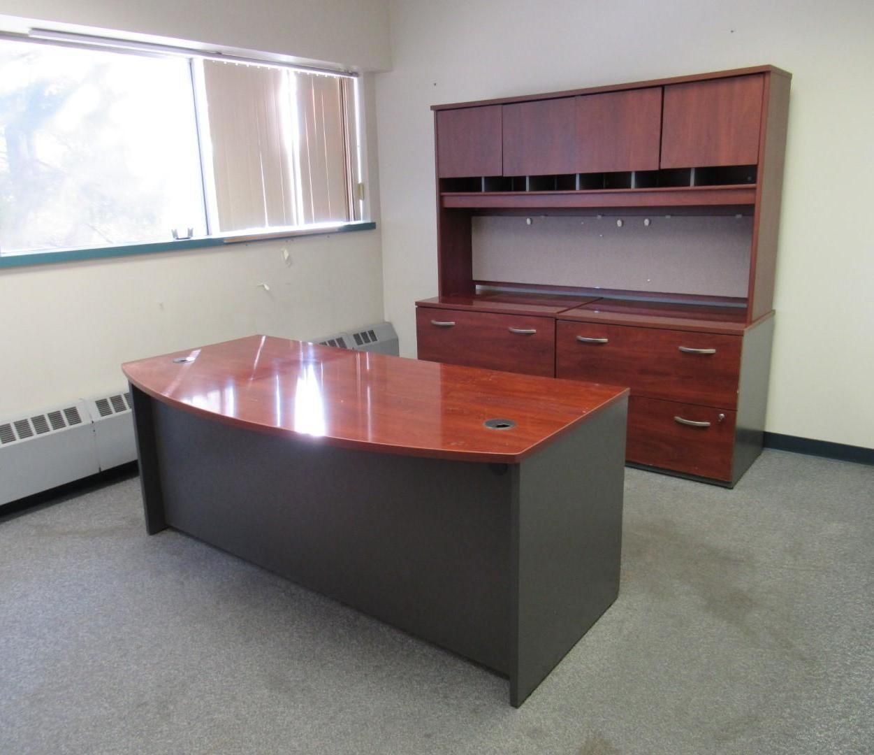 Office desk and hutch set, reddish-brown and gray. A curved desk sits in front of the hutch, near a window.
