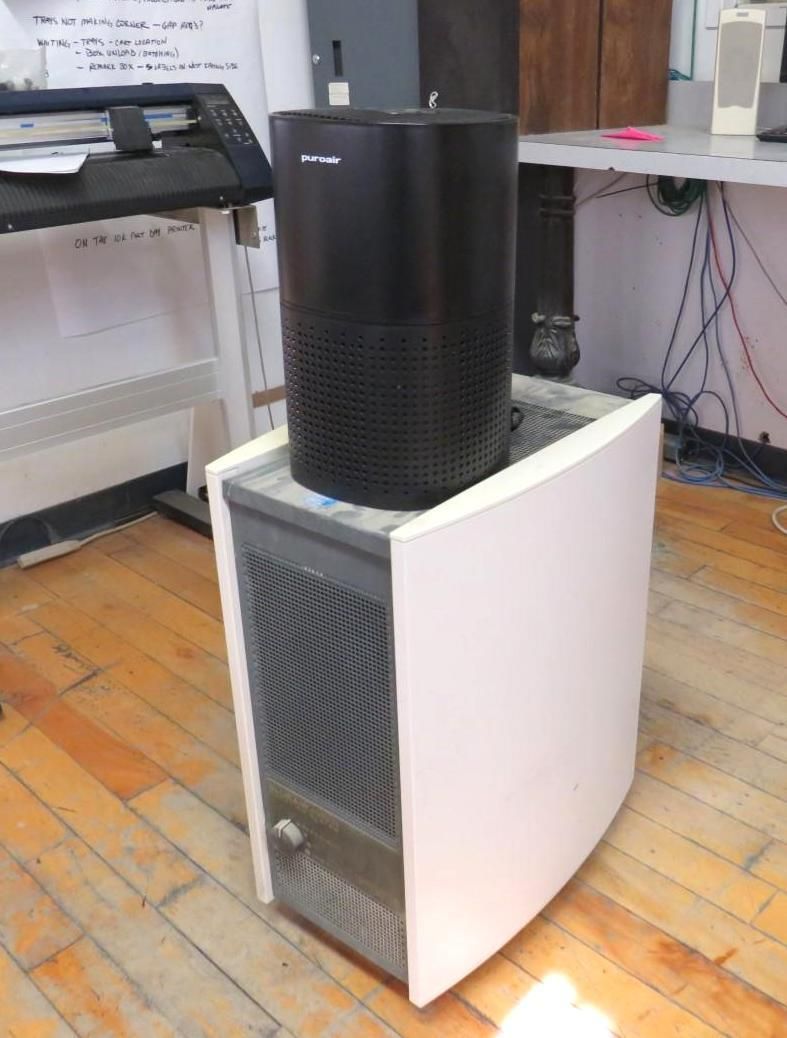 Black air purifier on top of a white computer tower on a wooden floor.
