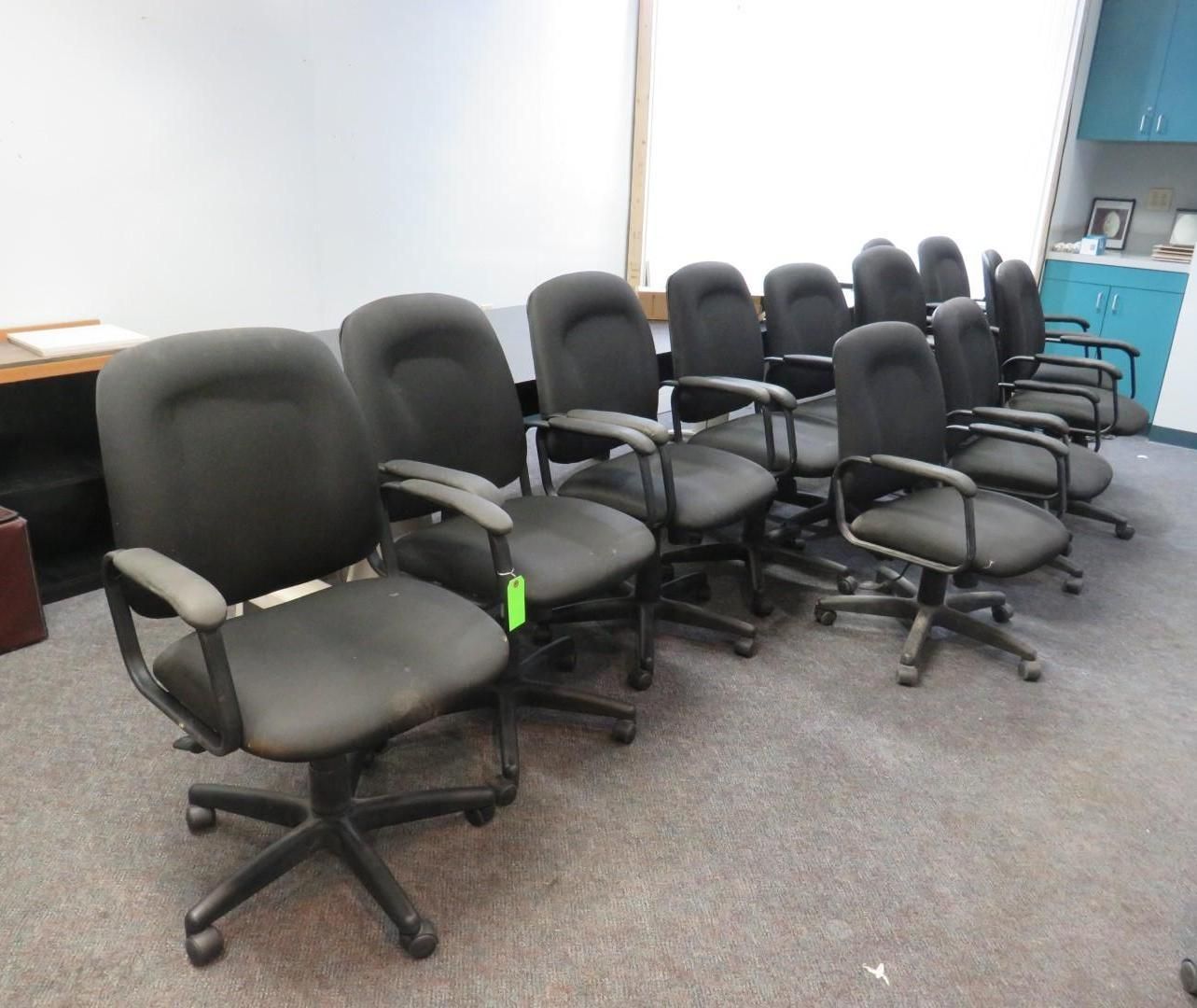 Office chairs lined up in a room, black with wheels and armrests.