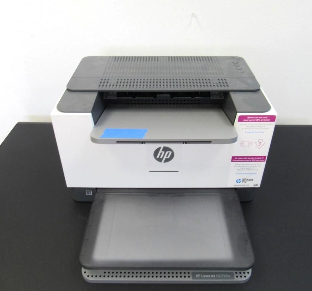 HP laser printer, white and gray, on a black surface. Paper tray is extended.