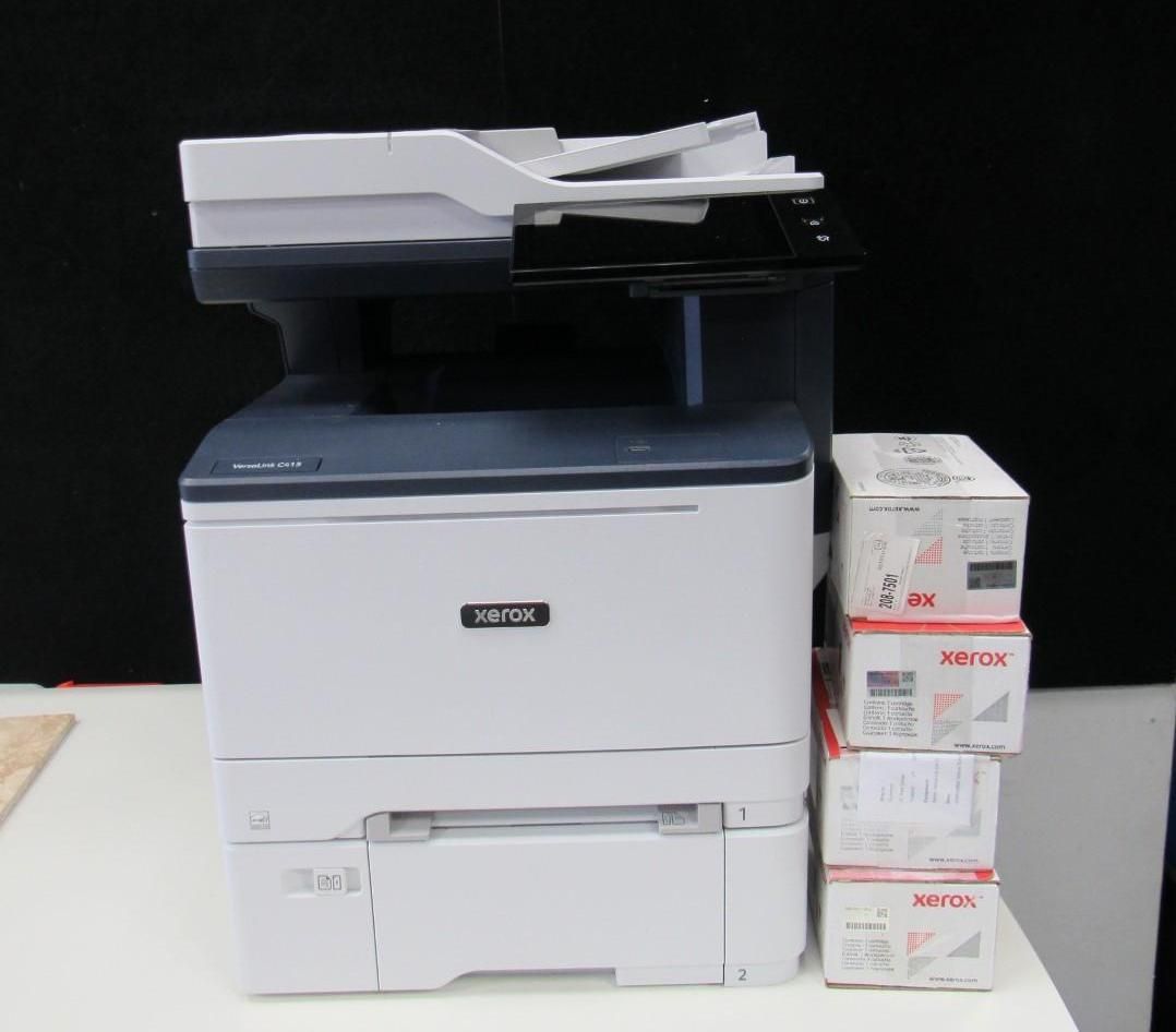 A white Xerox printer with a paper tray and stacked boxes of paper on a table.