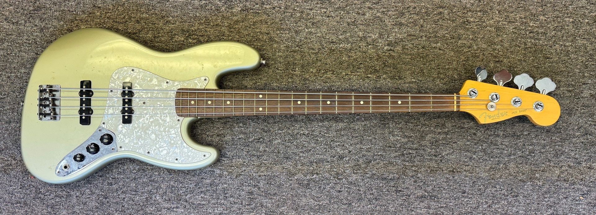 Yellow electric bass guitar on a gray carpet, with a maple neck and black pickups.