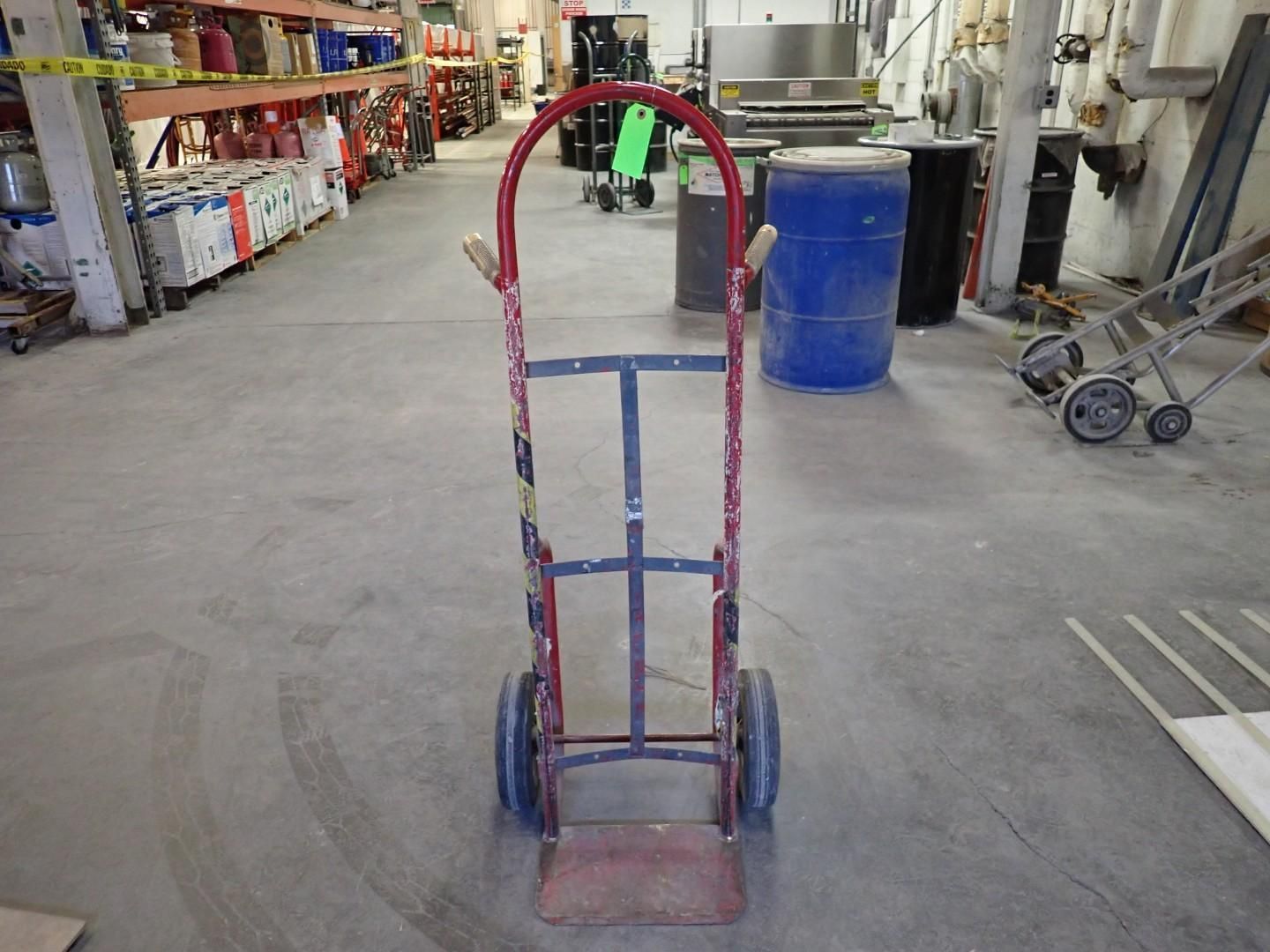Red hand truck in an industrial setting, with wheels, handle, and a load platform.