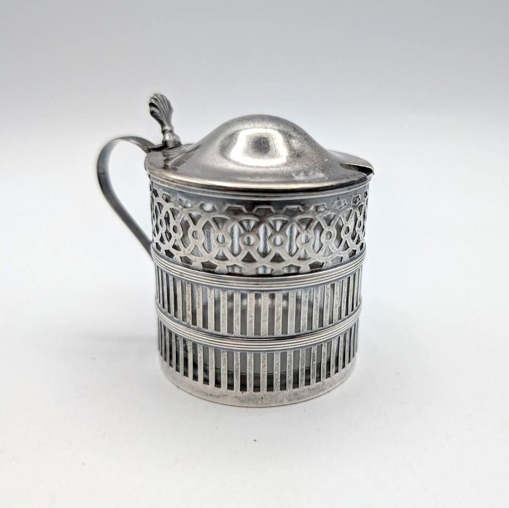 A silver-colored metal mustard pot or sugar jar with an intricate pierced lattice design and a lidded top.