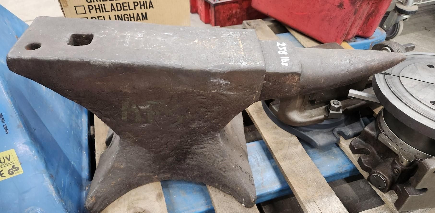 Anvil on a wooden pallet with other tools in a workshop.
