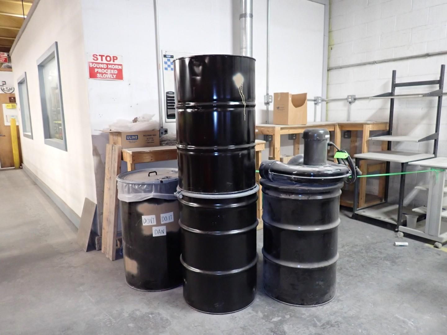 Black barrels stacked in an industrial setting, various sizes.