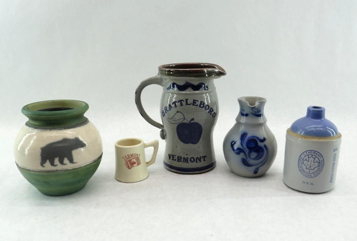 Five ceramic pitchers and vases on a white background: bear, miniature mug, apple motif, blue swirls, and bottle.