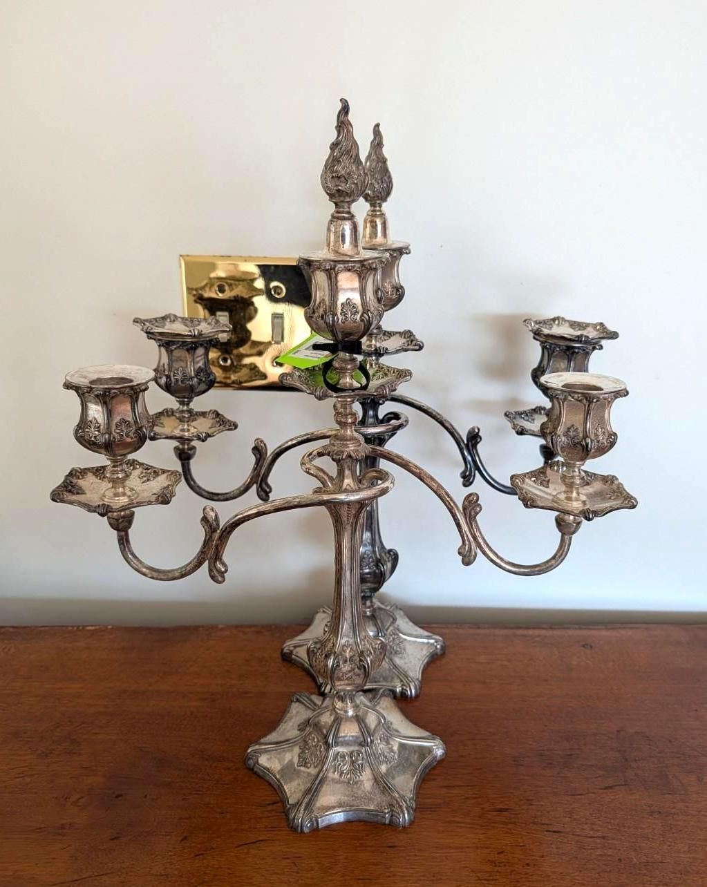 Two ornate silver candelabras stand on a wooden surface.