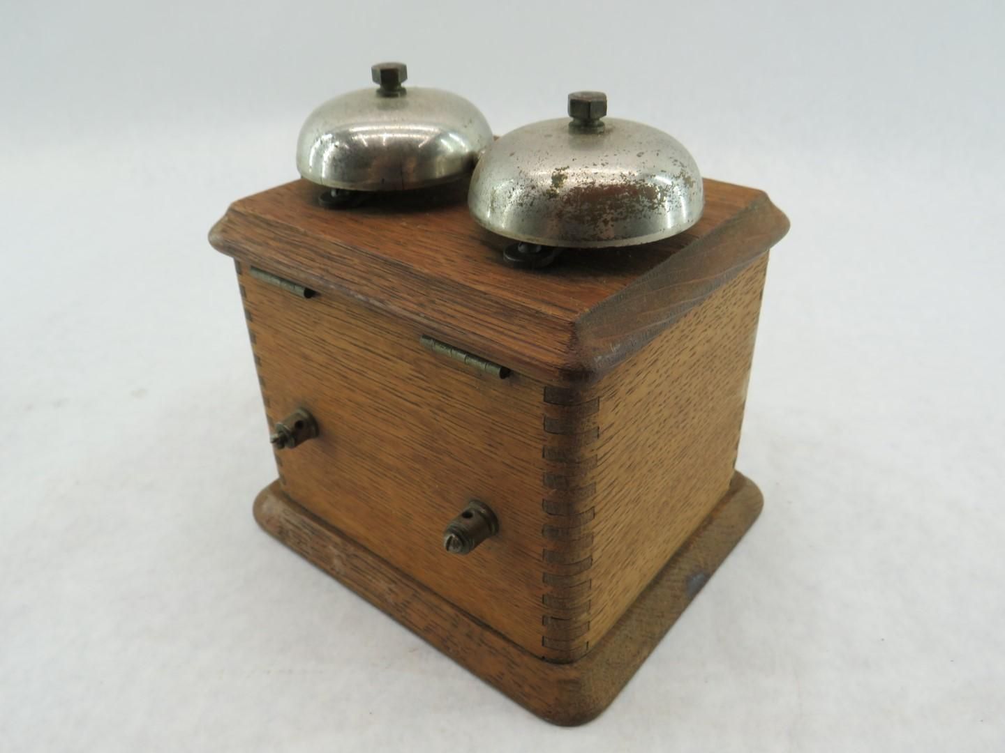Wooden box with two silver bells on top, two knobs on the side.